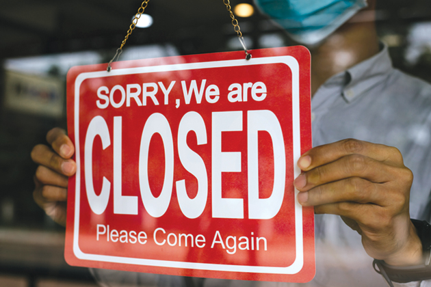A man wearing a COVID mask holds a sign in a shop window that says