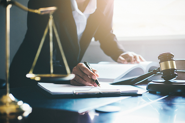 Person at desk referencing a book and writing something on a pad of paper