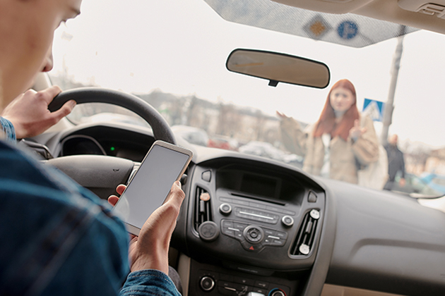Man looking at phone while driving and girl standing on street in front of his car